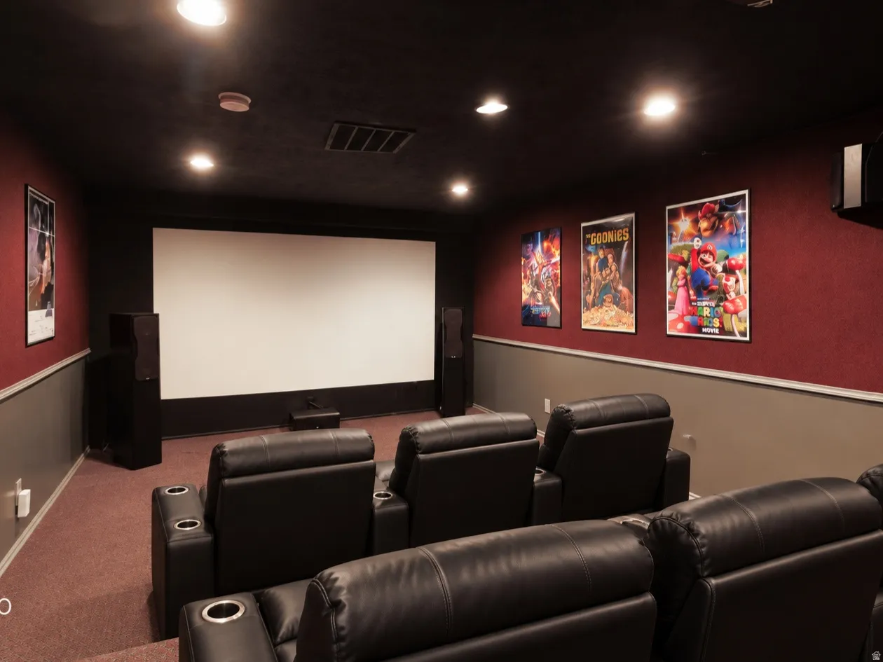 Dedicated home theater featuring a large projection screen, recessed ceiling lights, and wall-mounted speakers. Digitally staged furniture.