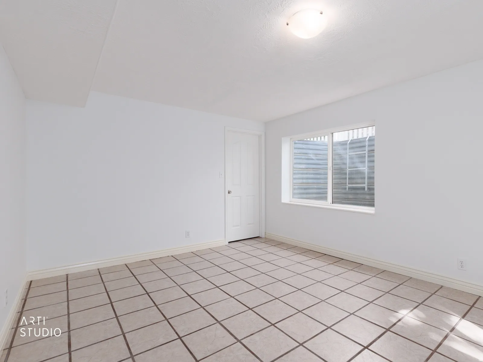 Spacious room featuring tile flooring, white walls, and a window with security bars