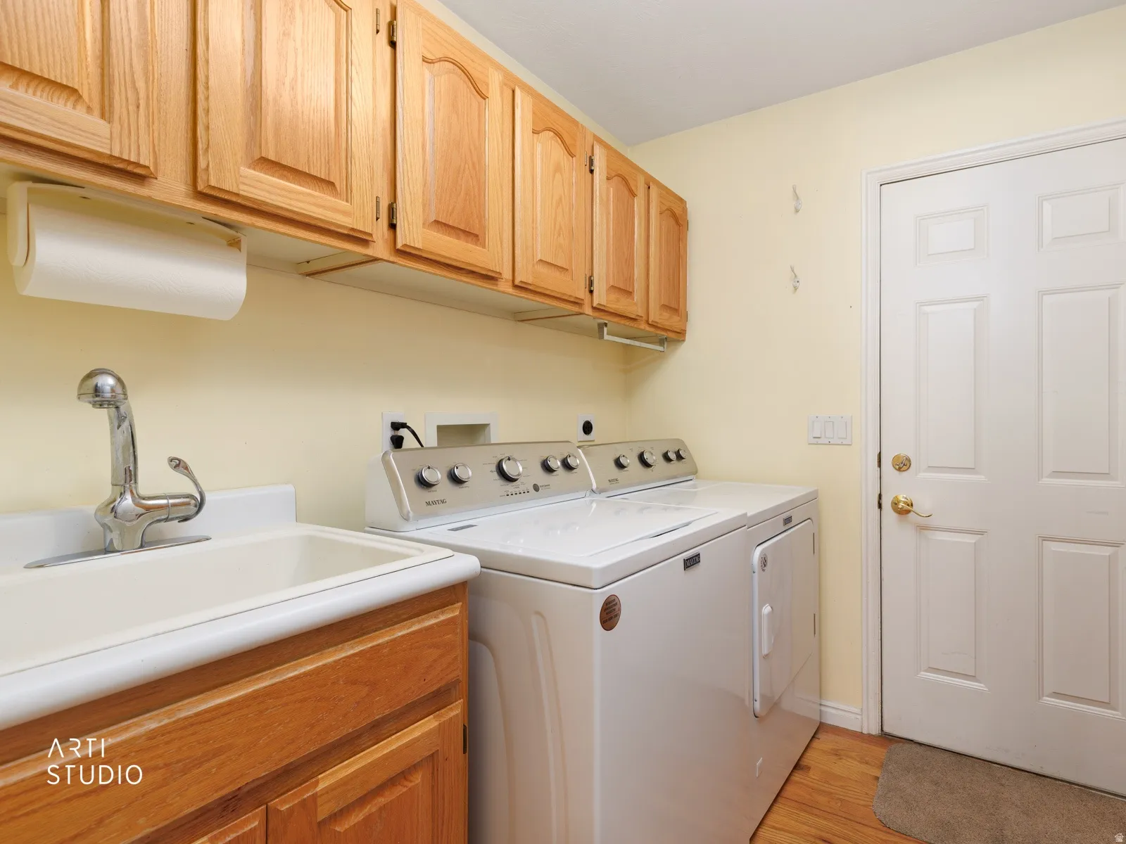 Laundry area featuring wood-finish flooring, light wood cabinetry, and a utility sink with a chrome faucet