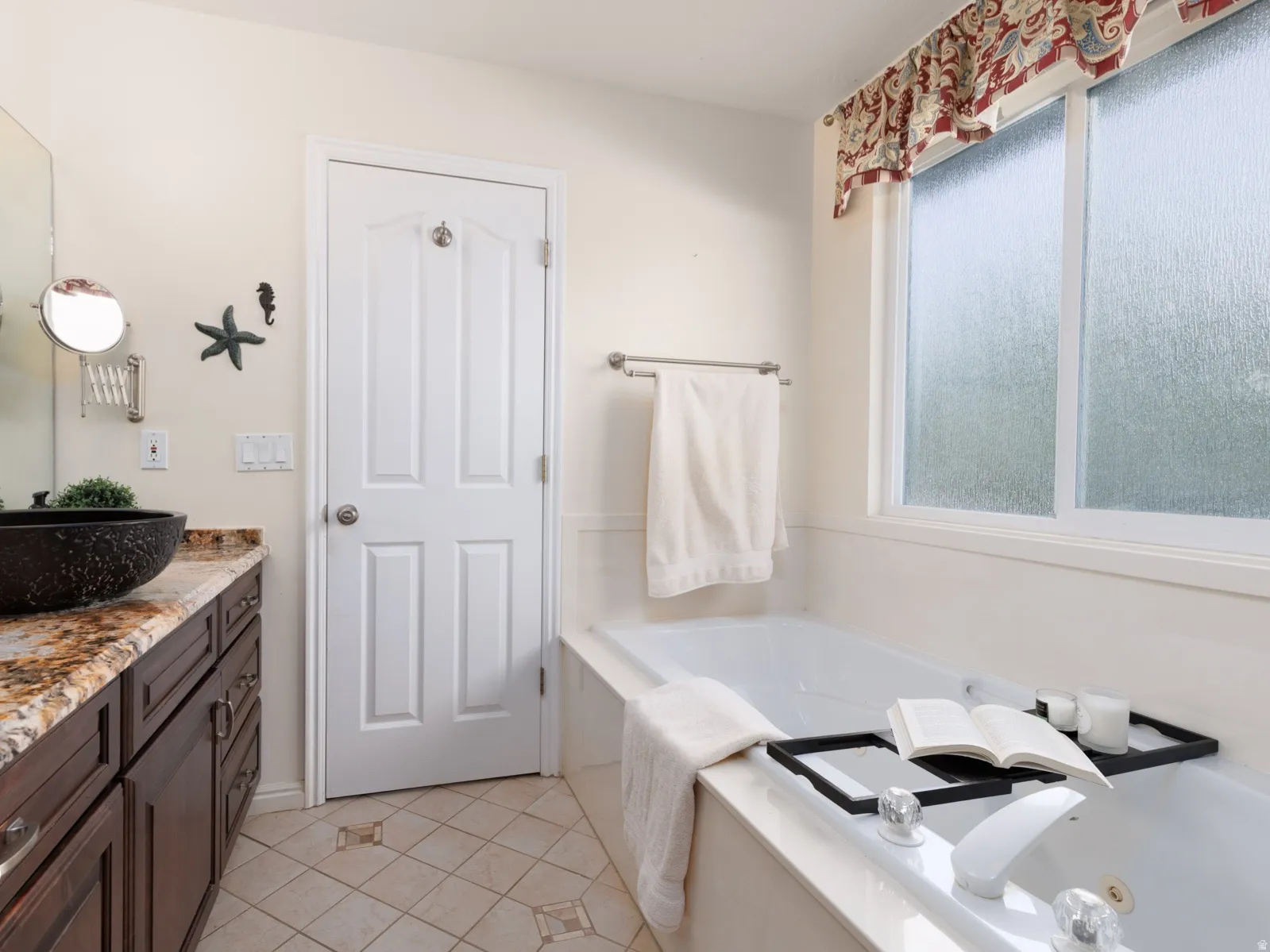 Expansive soaking tub with window, wood-finish vanity with stone countertop, and vessel sink with wall-mounted faucet