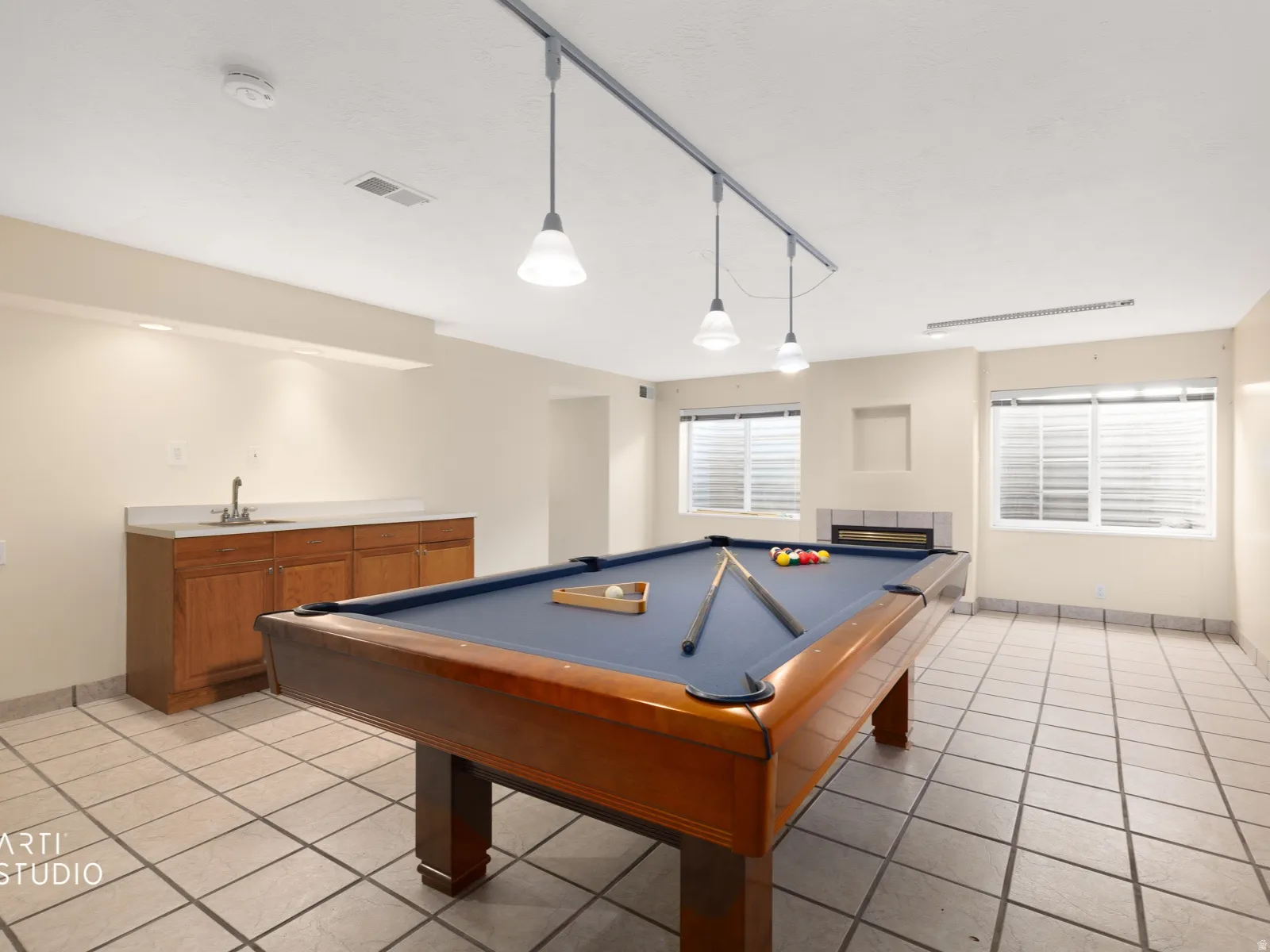 Spacious recreation area featuring tile flooring, a built-in wet bar with wood cabinetry and a solid surface countertop, multiple windows with blinds, and a built-in fireplace