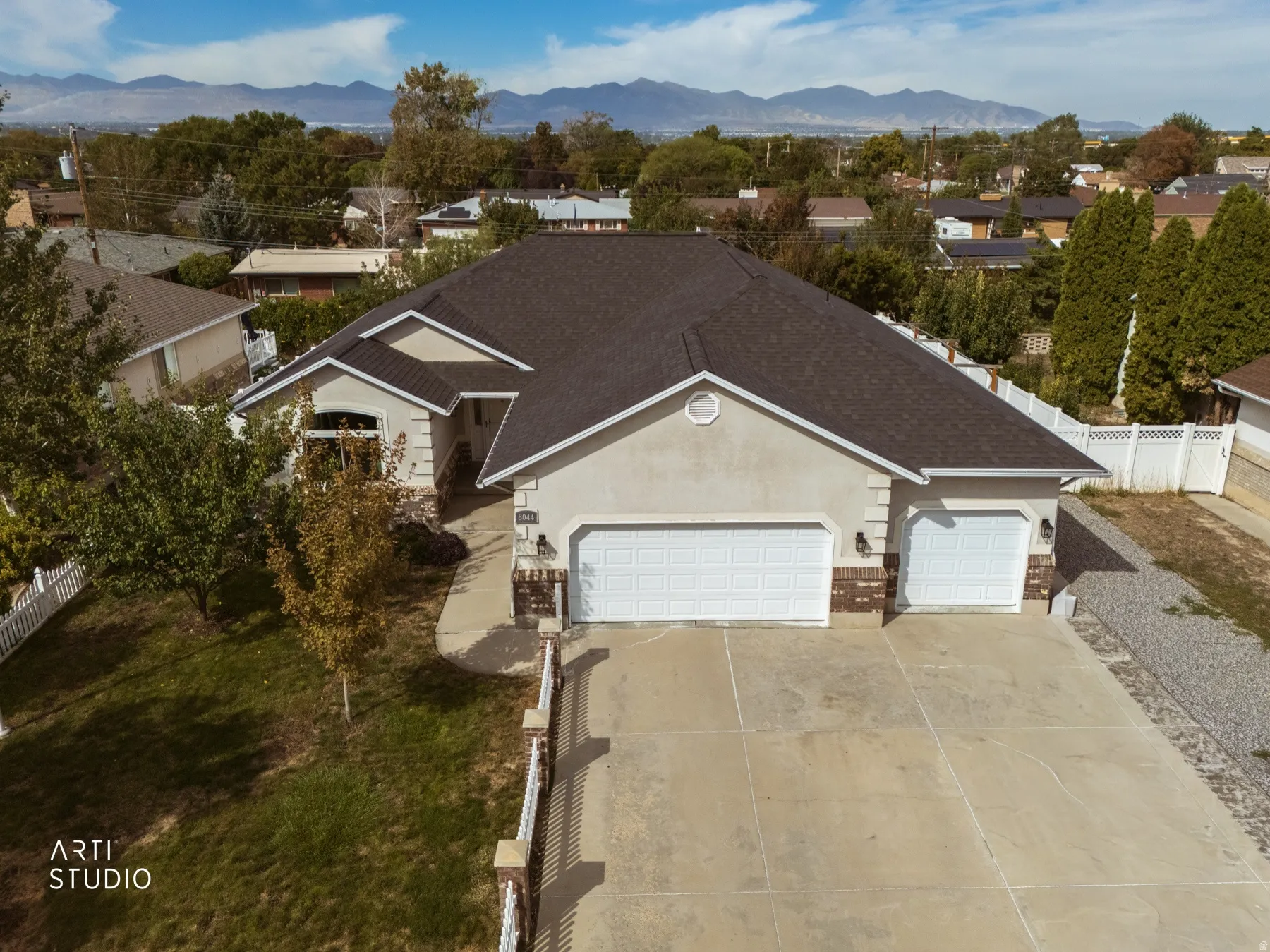Stucco exterior with brick accents, attached multi-car garage, concrete driveway, and mature landscaping