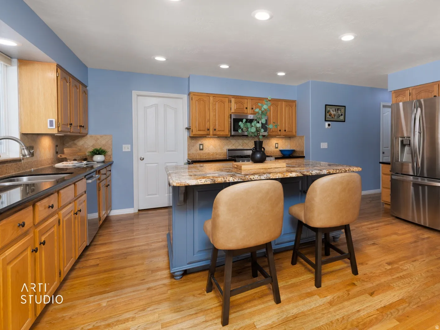 Kitchen featuring a central island with countertop seating, stainless steel appliances, wood-finish flooring, recessed lighting, and a double basin sink