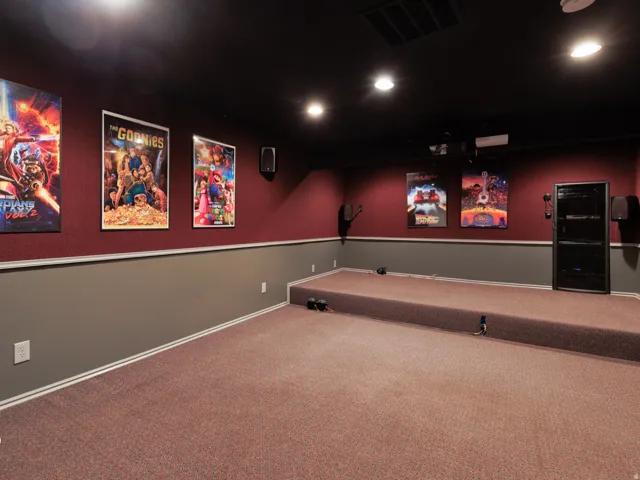 Theatre room with tiered carpeting, built-in projector, recessed lighting, wall-mounted speakers, and a two-tone wall treatment