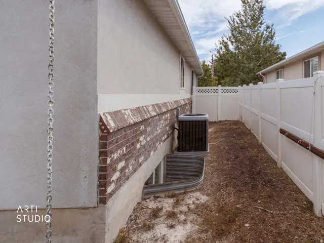 Property exterior featuring stucco siding, brick detailing, a window well, and a white privacy fence