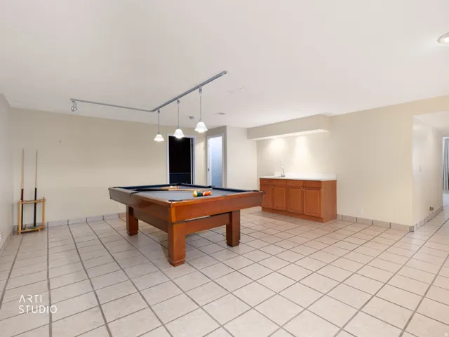 Spacious room with light-toned tile flooring, track lighting, and a built-in wood-finish cabinet with a light-toned countertop