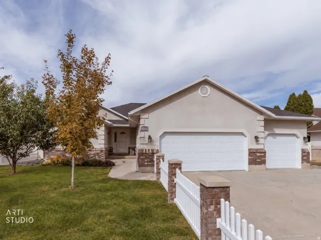 Stucco exterior with brick accents, attached multi-car garage, concrete driveway, white picket fence, and established landscaping