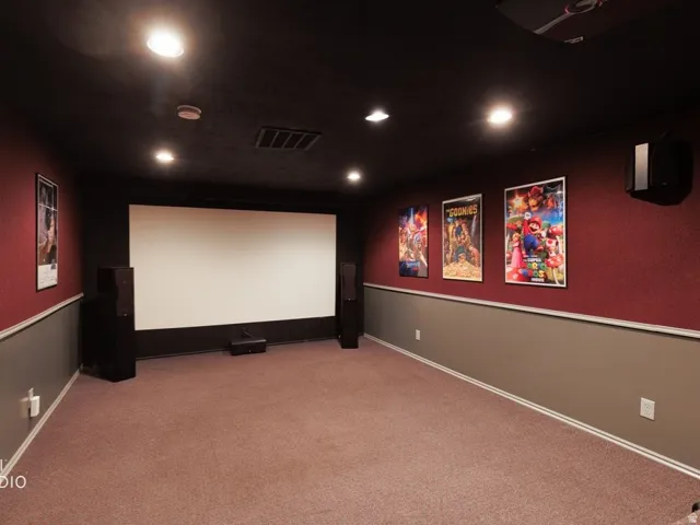 Dedicated media room featuring a large projection screen, recessed lighting, and wall-mounted speakers