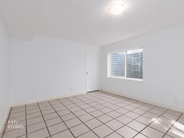 Spacious room featuring tile flooring, white walls, and a window with security bars