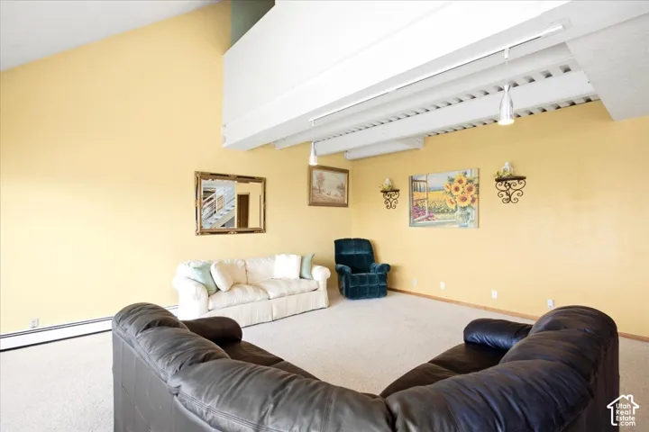 Spacious living area featuring a vaulted ceiling, exposed white beams, and wall-mounted light fixtures