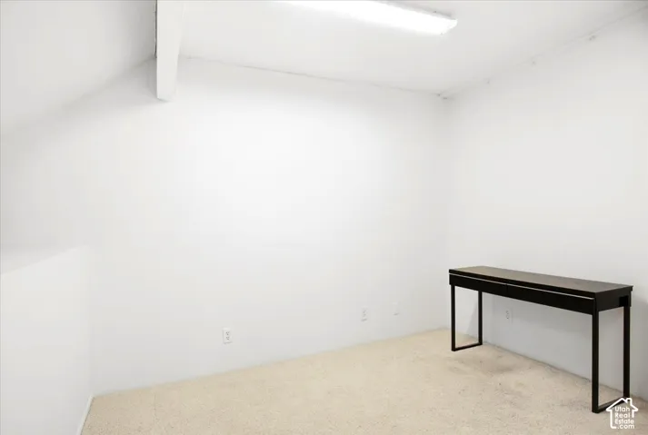 White walls with an angled ceiling beam and light-toned carpeting