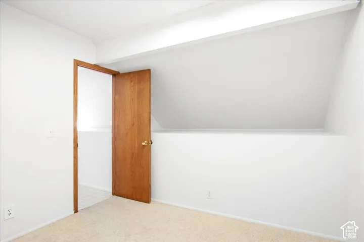 White walls with an angled ceiling feature, wood-finish interior door, and light-toned carpeting