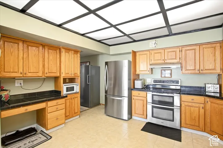 Recessed panel wood cabinetry, tile countertops, stainless steel double oven, stainless steel refrigerator, and tiled flooring