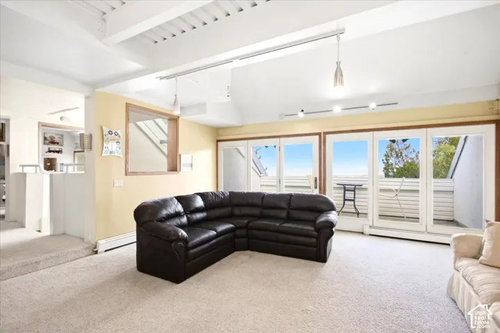 Vaulted ceiling with exposed beams, carpeted flooring, and a bank of glass panel doors