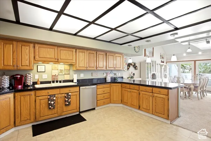 Kitchen featuring wood cabinetry, black countertops, stainless steel dishwasher, and tile flooring