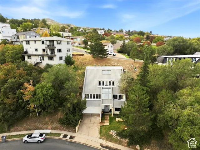 Multi-level residence with a metal roof and light-colored siding, integrated garage, and mature surrounding trees