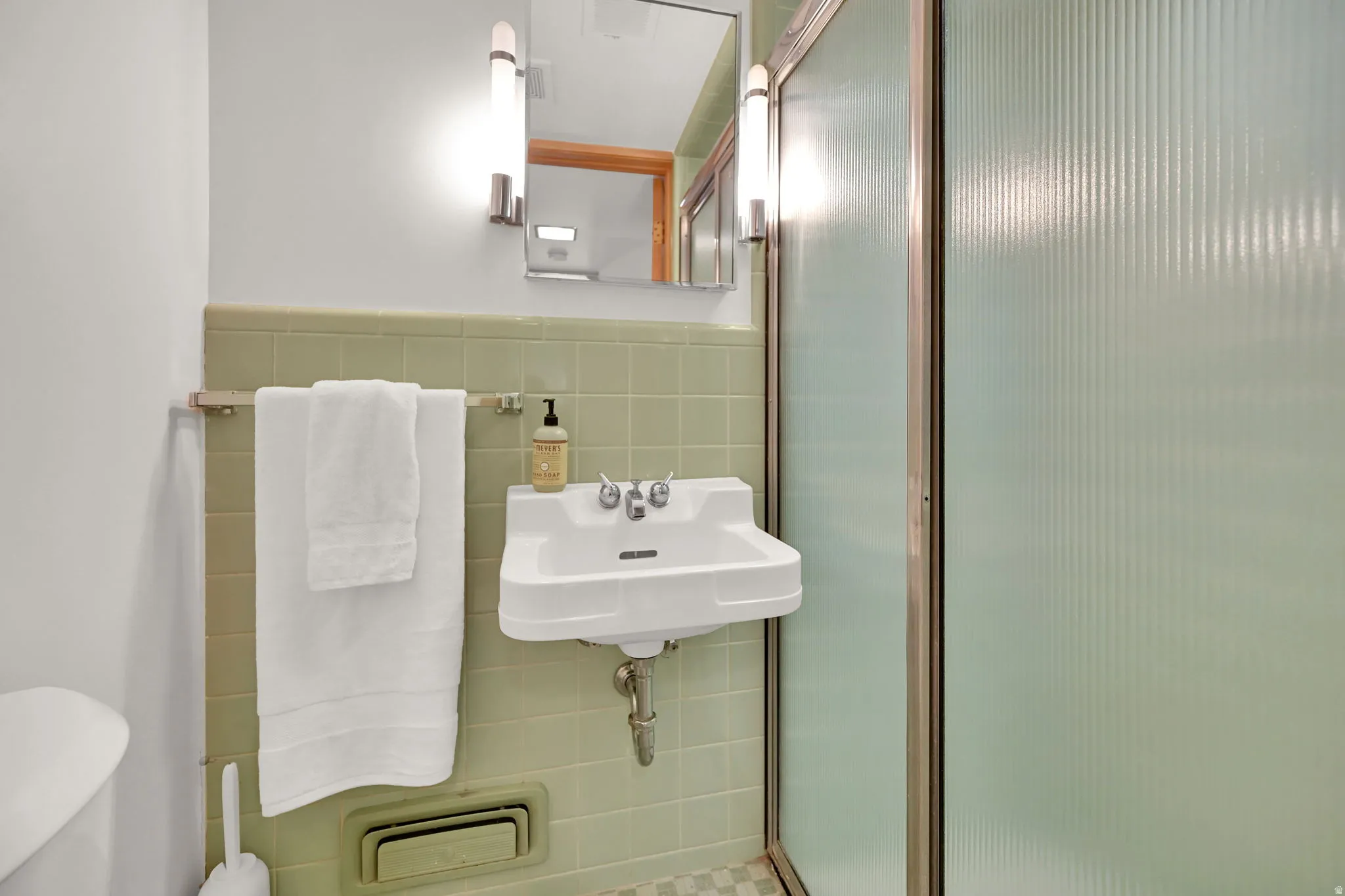 Wall-mounted sink with chrome fixtures, full-height wall tiling, and a shower enclosure with frosted glass panels