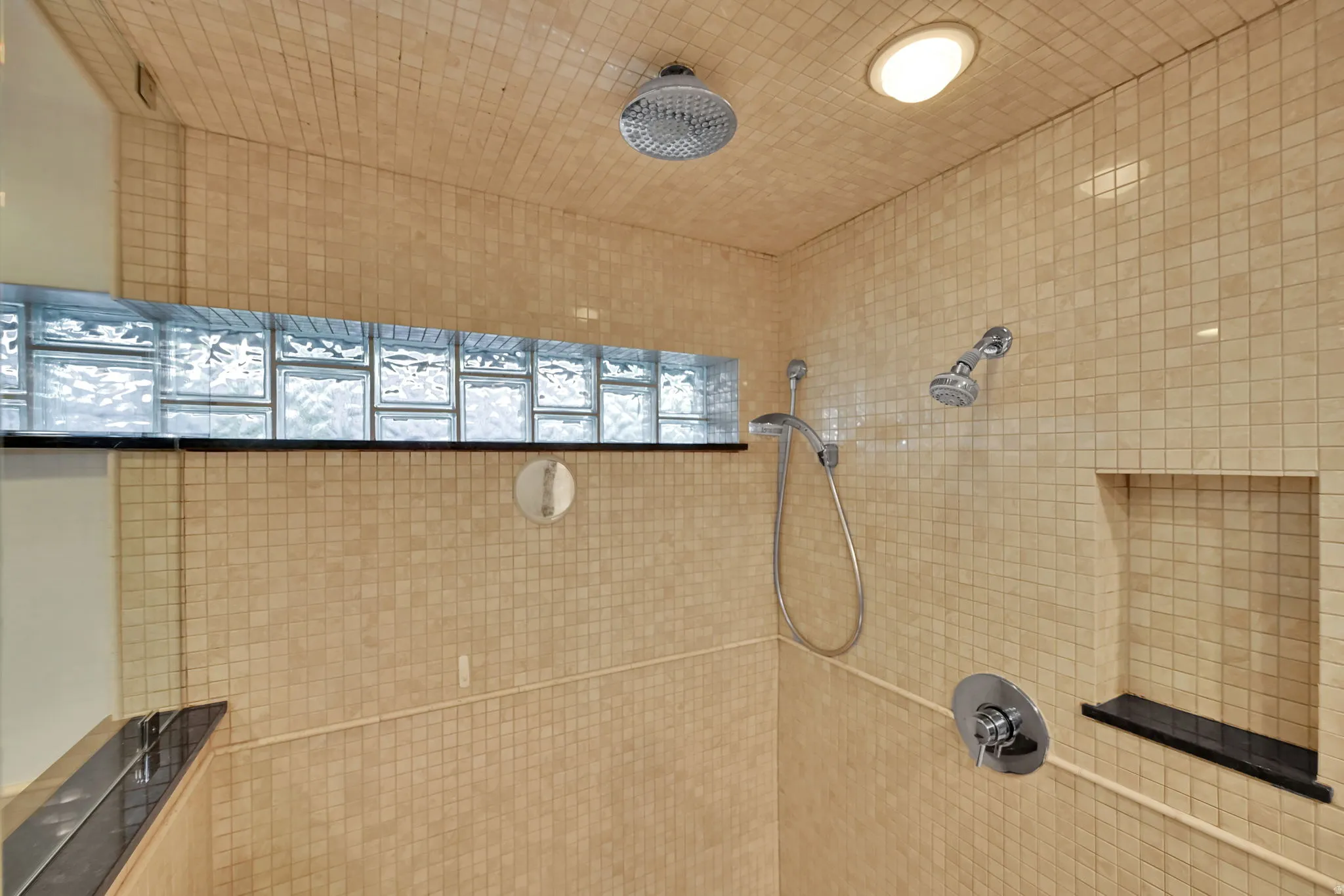 Shower featuring full-height mosaic tile, recessed lighting, glass block window, built-in shelf, and dual shower heads