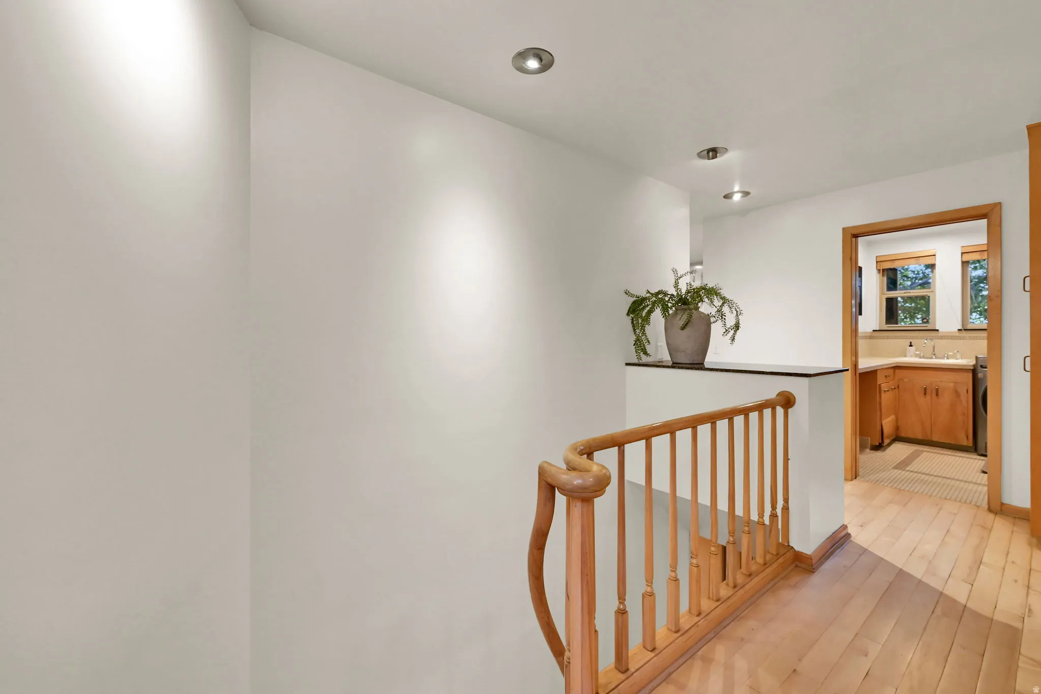Wood-finish flooring with a natural wood staircase railing and recessed ceiling lighting