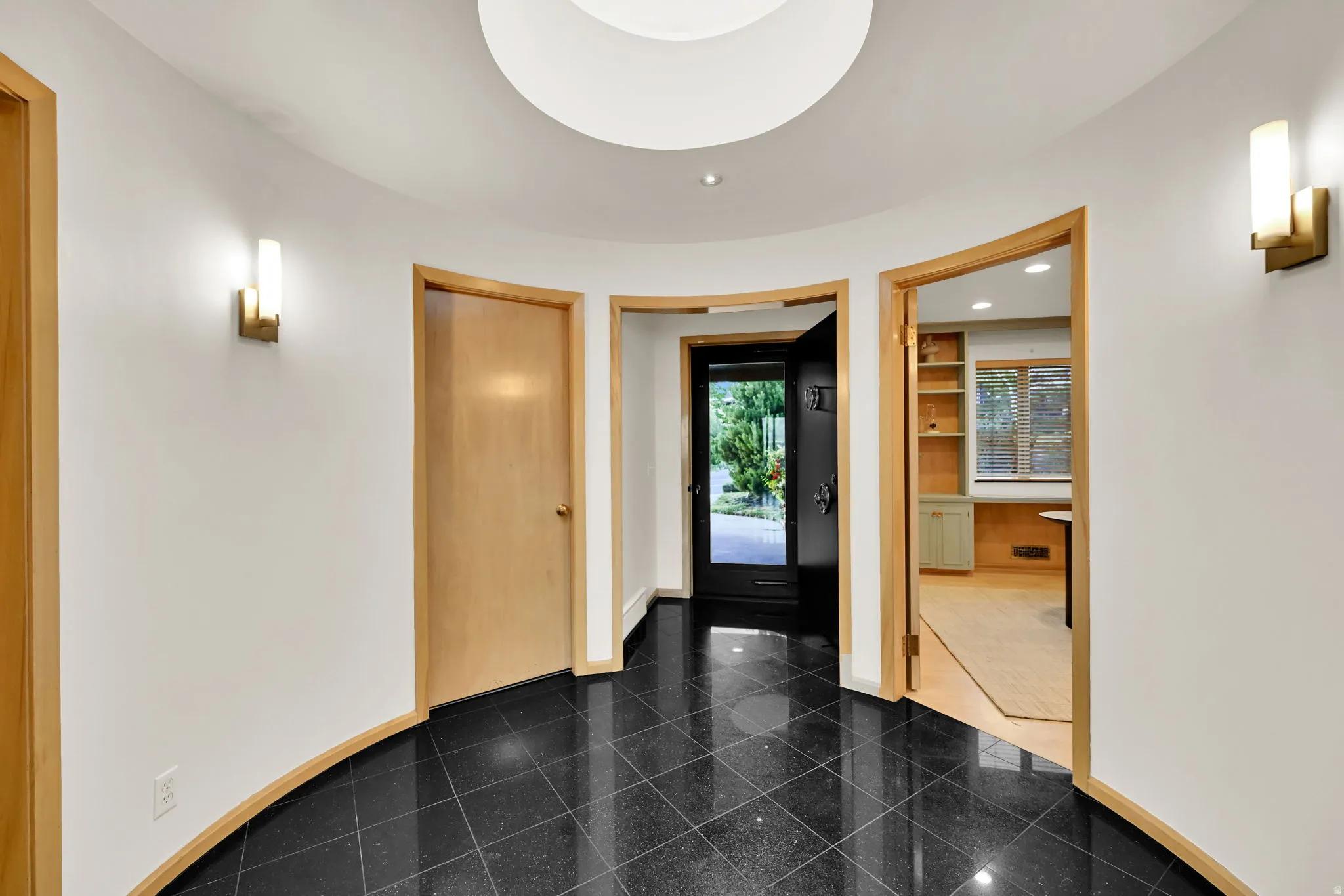 Curved entryway featuring black tile flooring, recessed lighting, and modern wall sconces