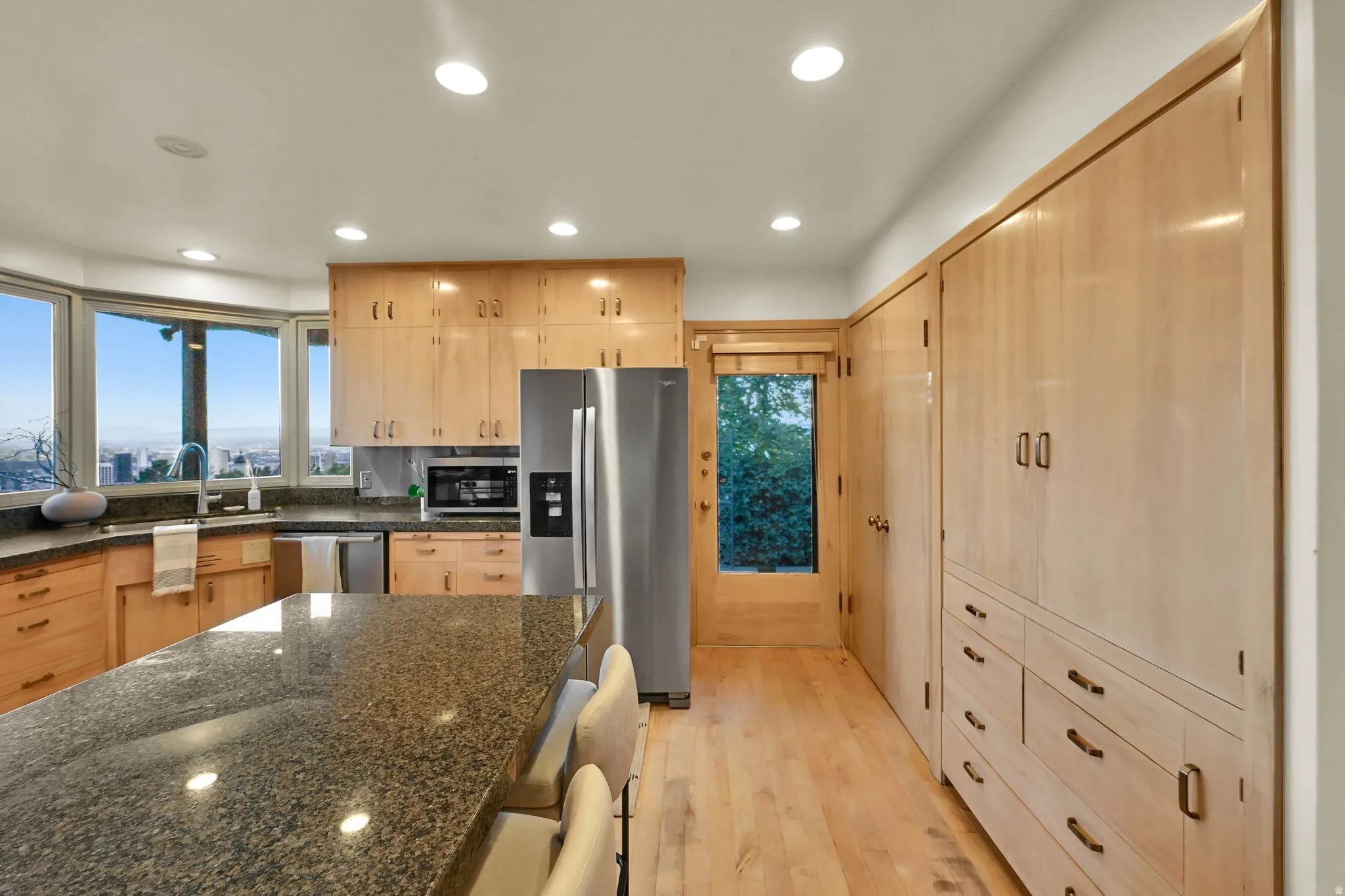 Kitchen featuring abundant light wood cabinetry, stainless steel appliances, a large center island with a stone countertop, and a built-in storage wall