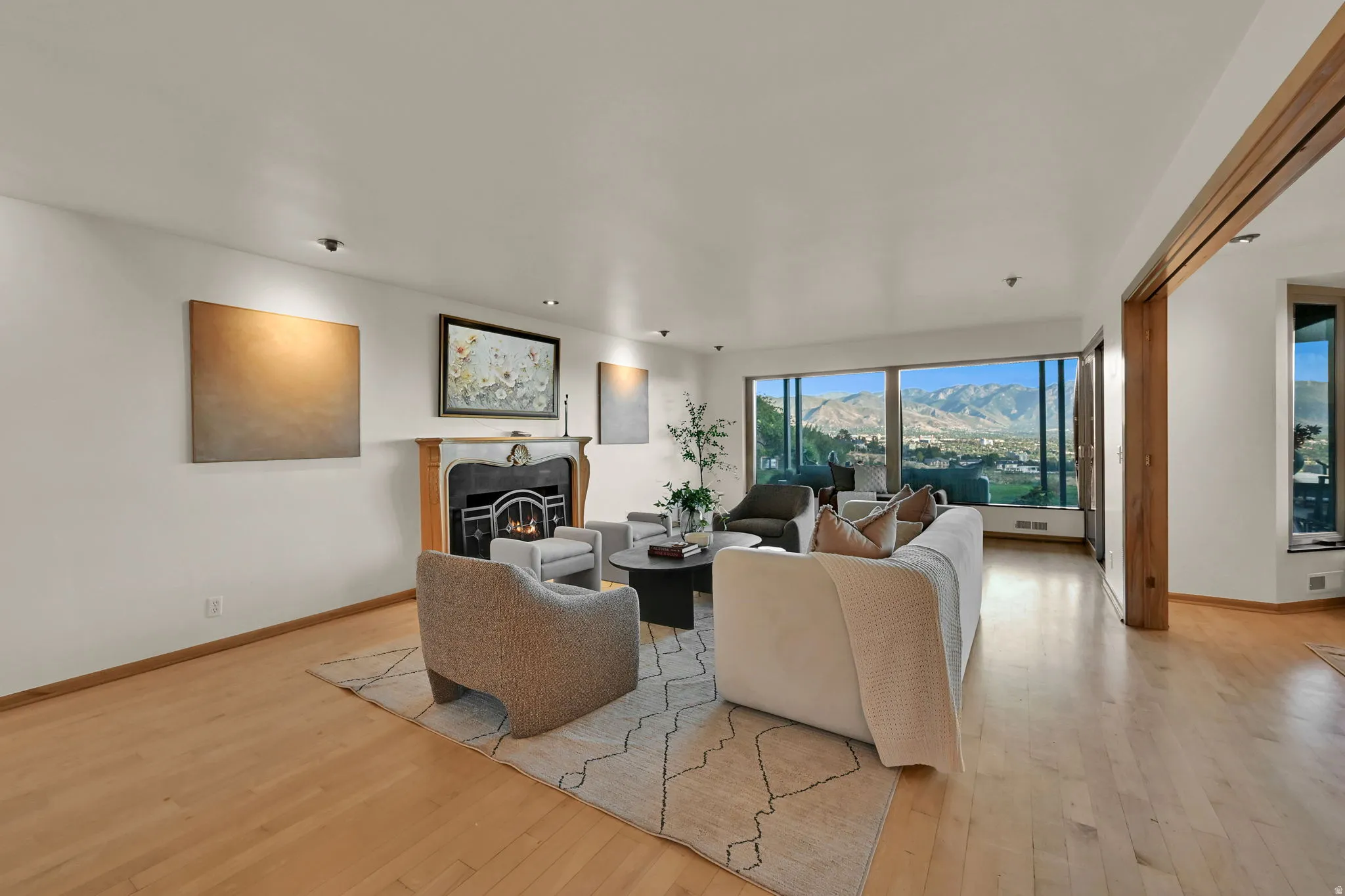 Hardwood flooring, a fireplace with a detailed mantel, recessed lighting, and expansive windows showcasing a mountain backdrop