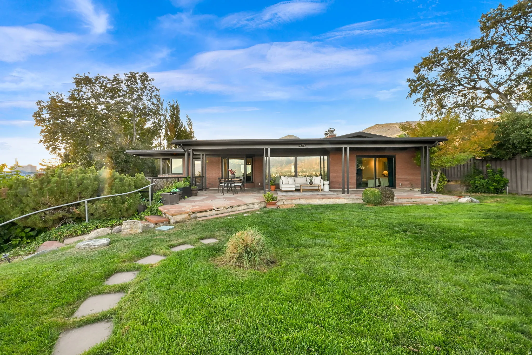 Expansive terraced yard with a stone path, mature trees, and a patio featuring a covered area