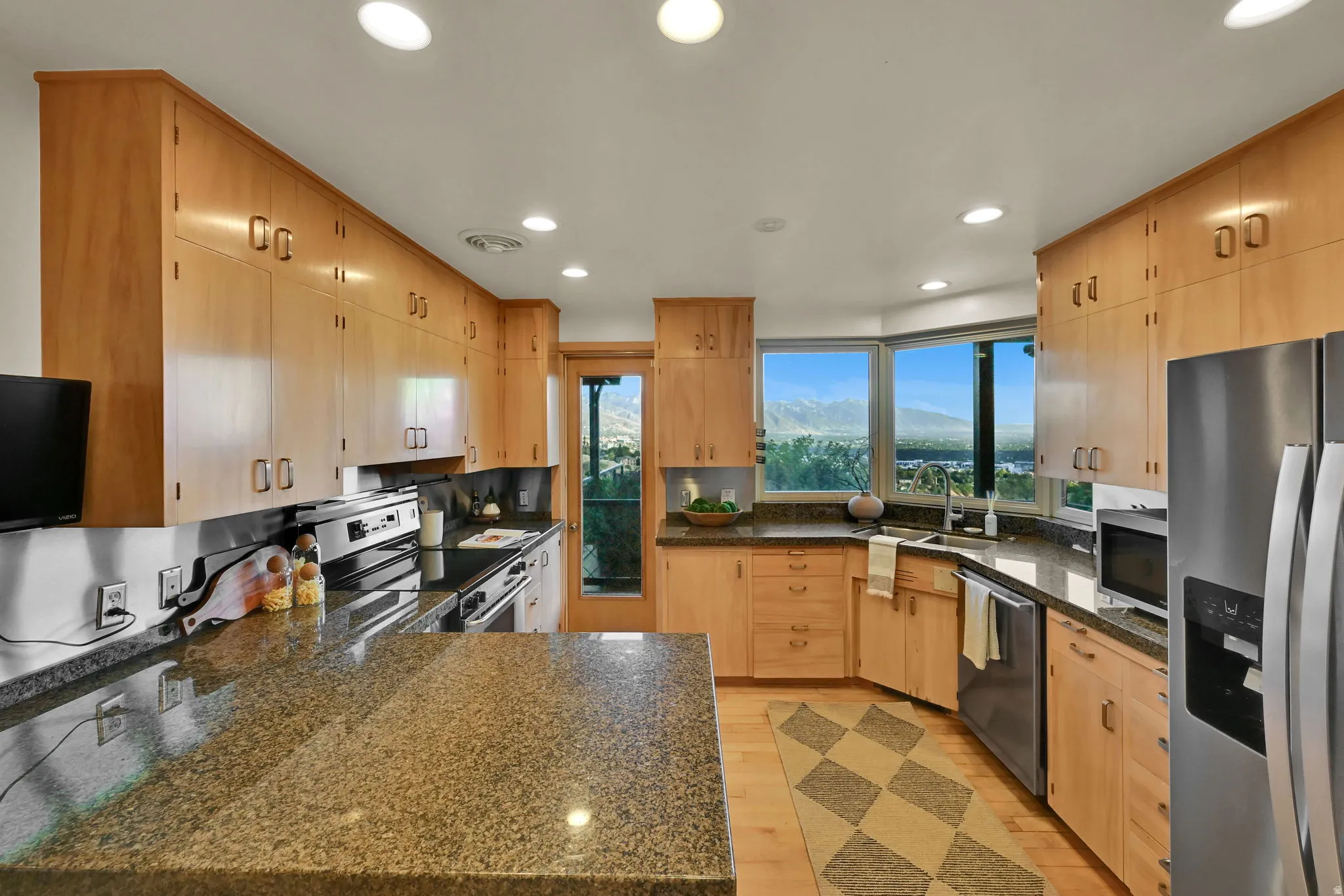 Kitchen featuring extensive light wood cabinetry, stone countertops, stainless steel appliances, and wood-finish flooring