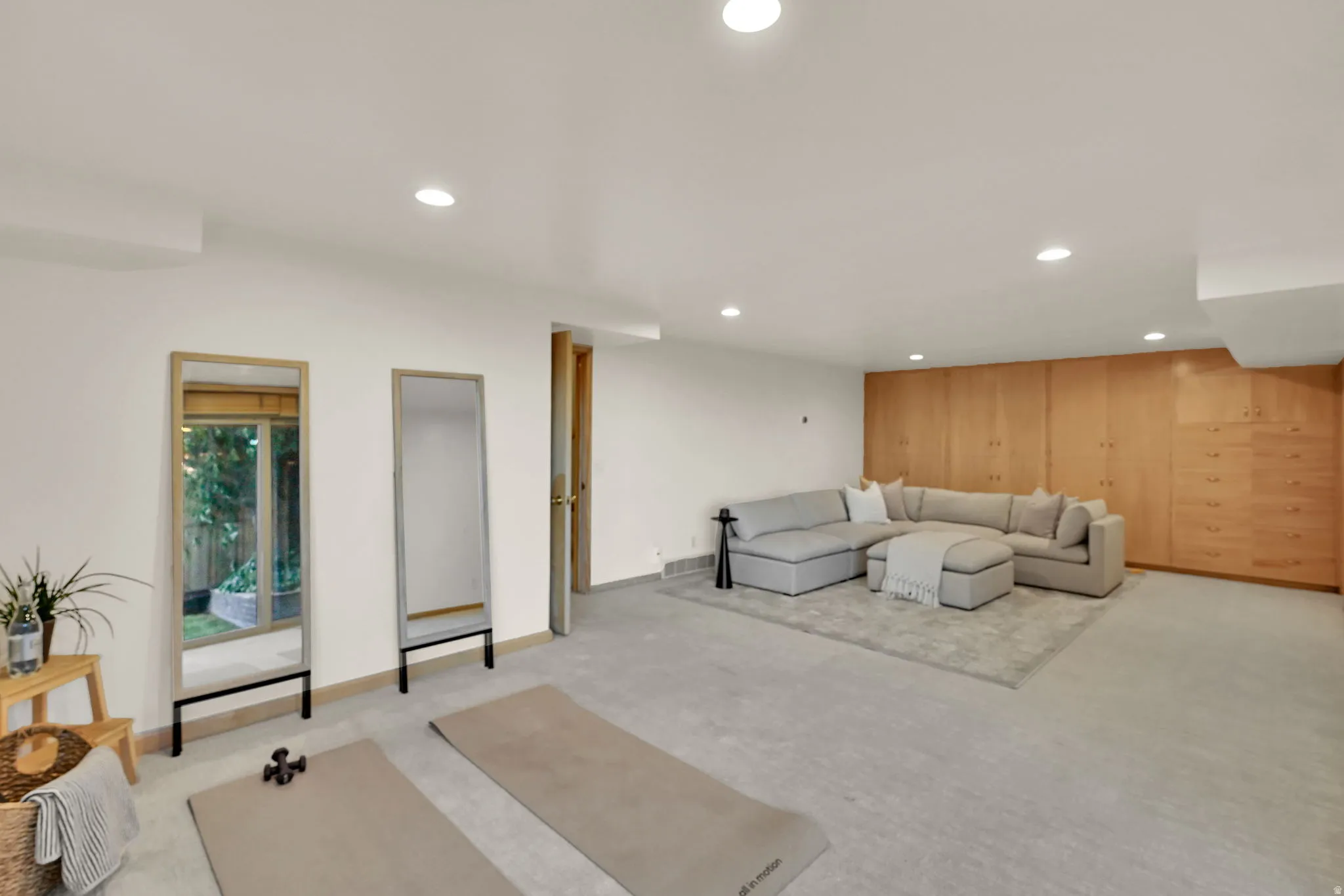 Recessed lighting illuminates the spacious room featuring extensive built-in wood cabinetry and a neutral carpeted floor