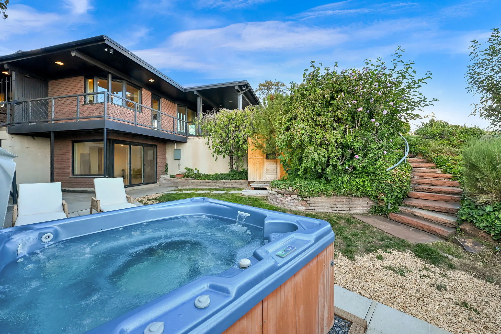 Ground-level patio with an outdoor spa, terraced landscaping with stone steps, and a multi-level deck