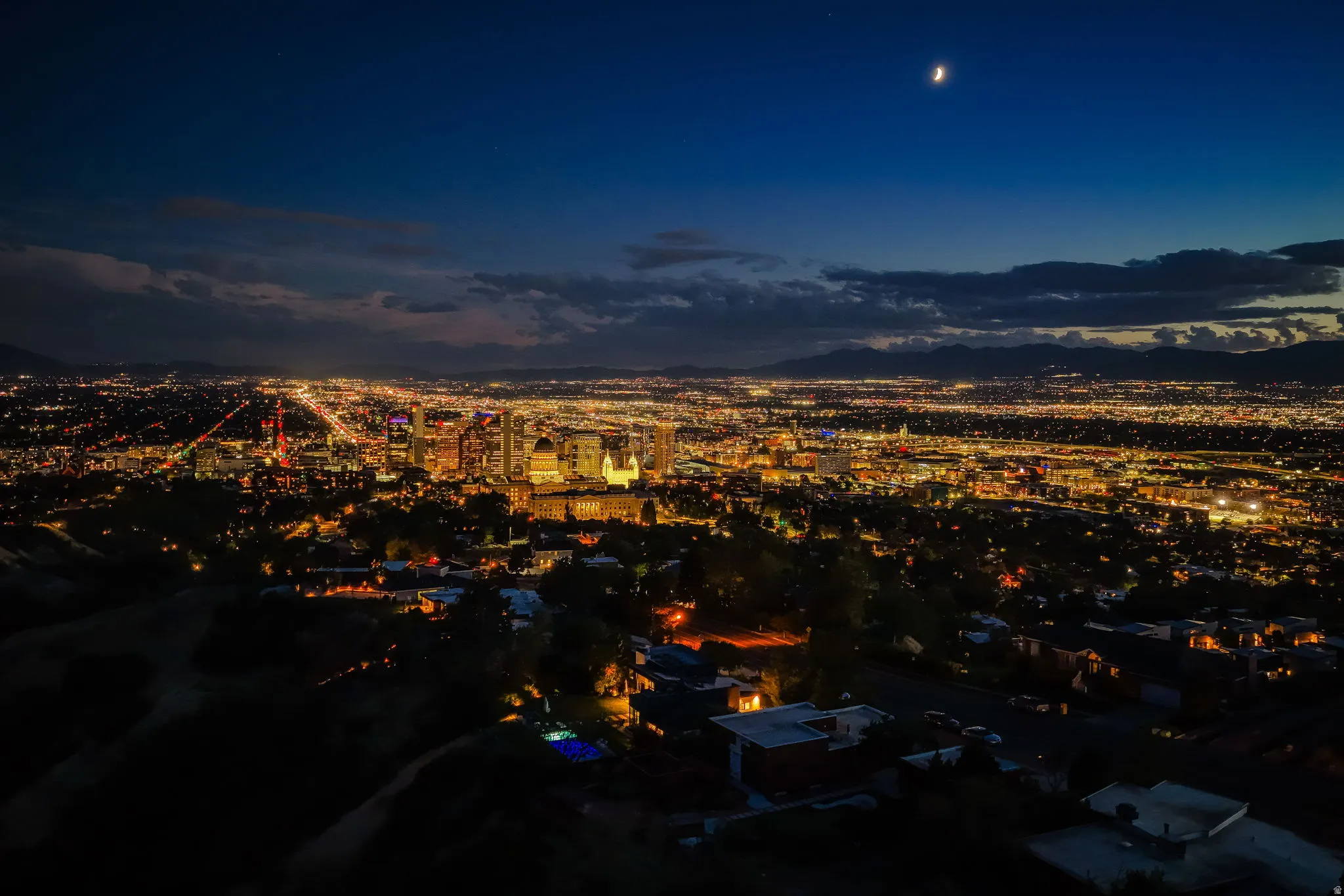 Panoramic cityscape at night with illuminated buildings and surrounding mountains