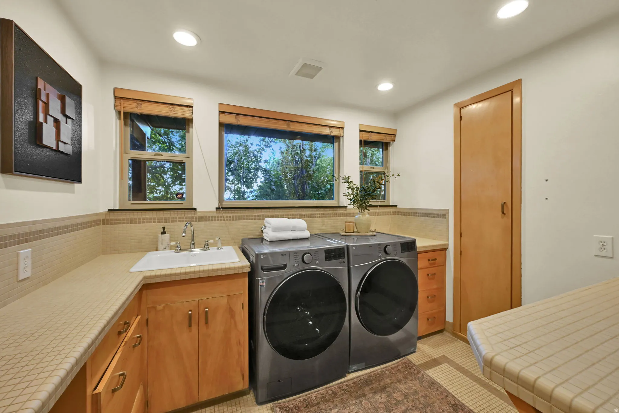 Laundry room featuring a built-in sink, wood cabinetry, tiled countertops, and multiple windows