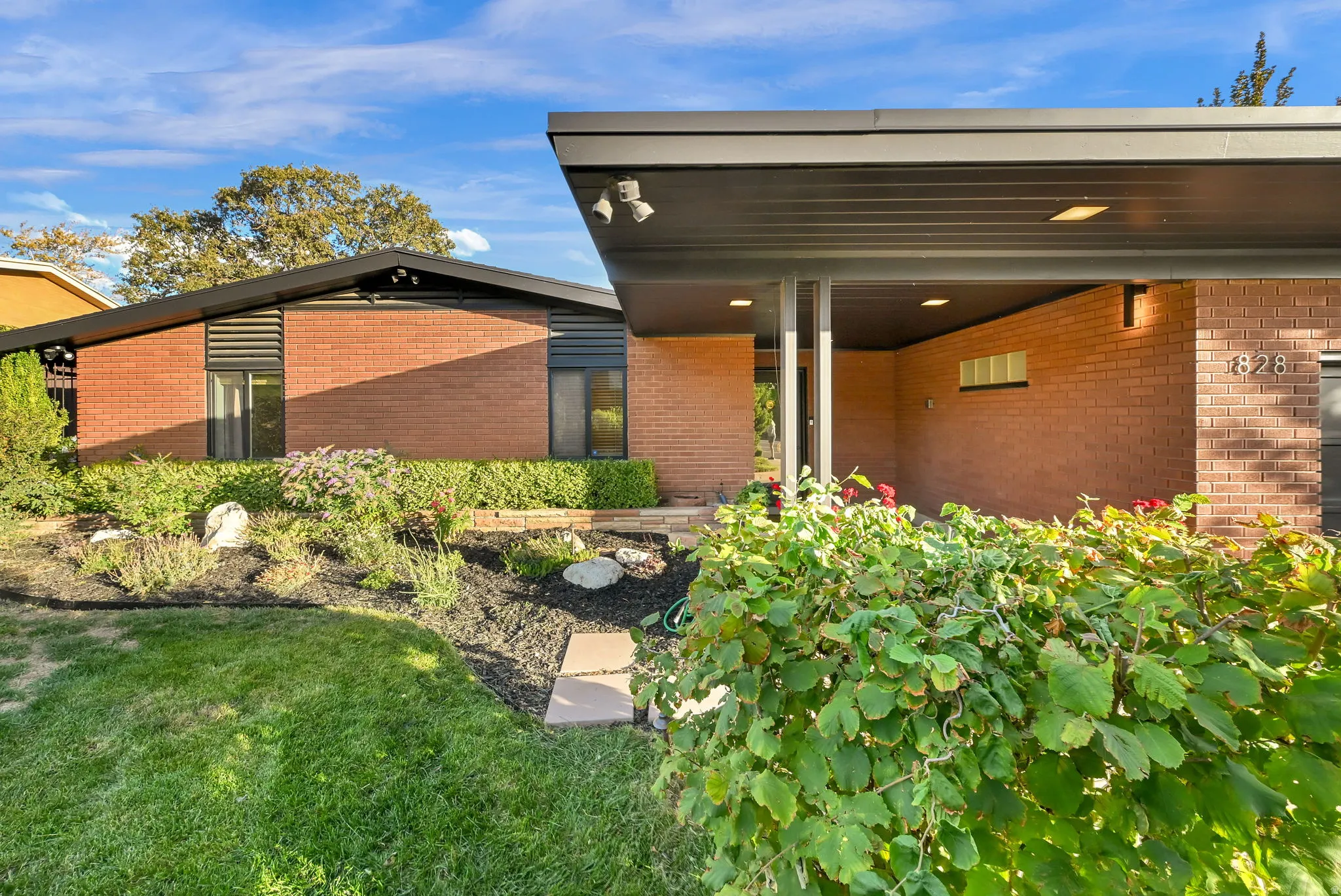Mid-century modern residence featuring brick exterior, a covered entry, and a manicured front yard