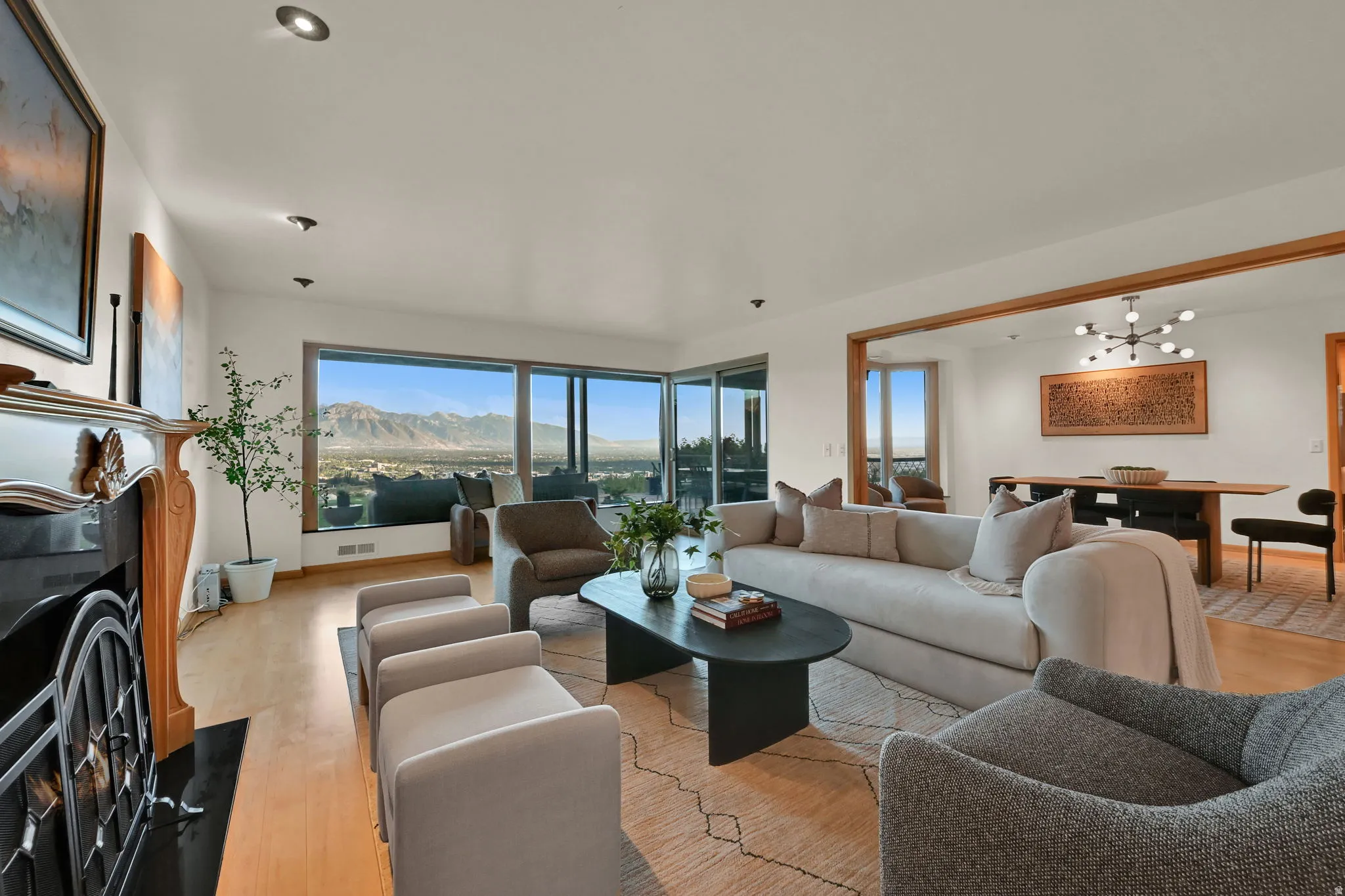 Expansive living area featuring wood-finish flooring, a traditional fireplace with a black surround, recessed lighting, and large windows showcasing mountain scenery