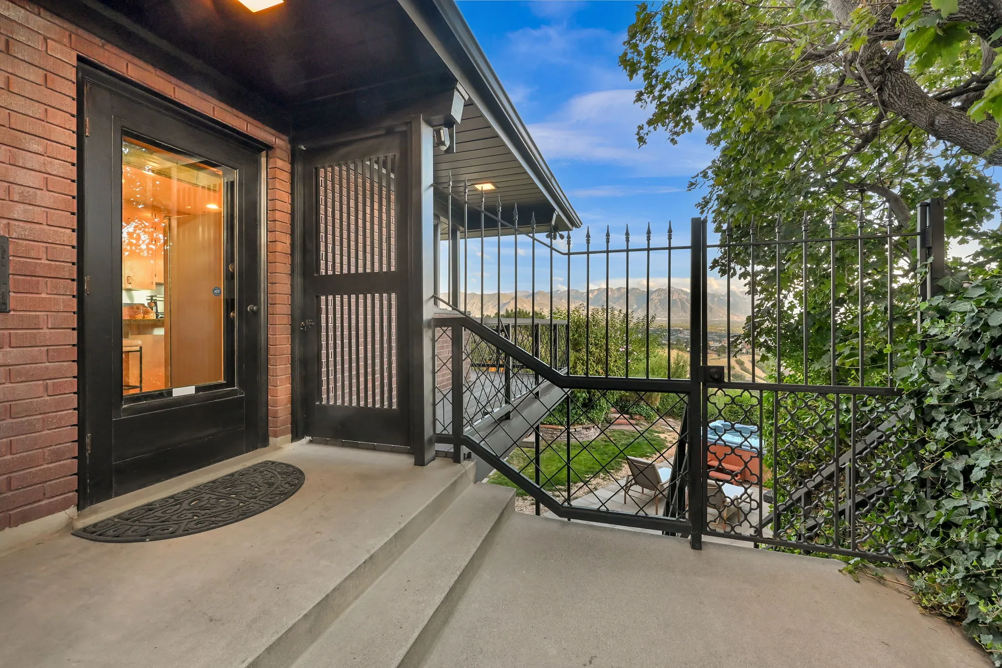 Brick exterior with a black framed glass entry door, concrete steps, and a decorative wrought iron gate