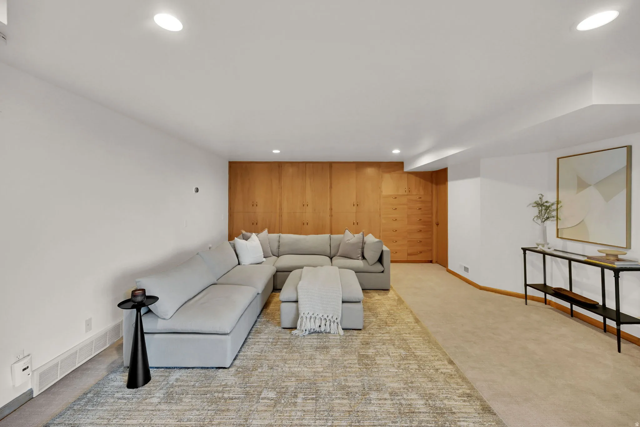 Recessed ceiling lighting illuminates a spacious room featuring a wood-paneled accent wall with integrated storage