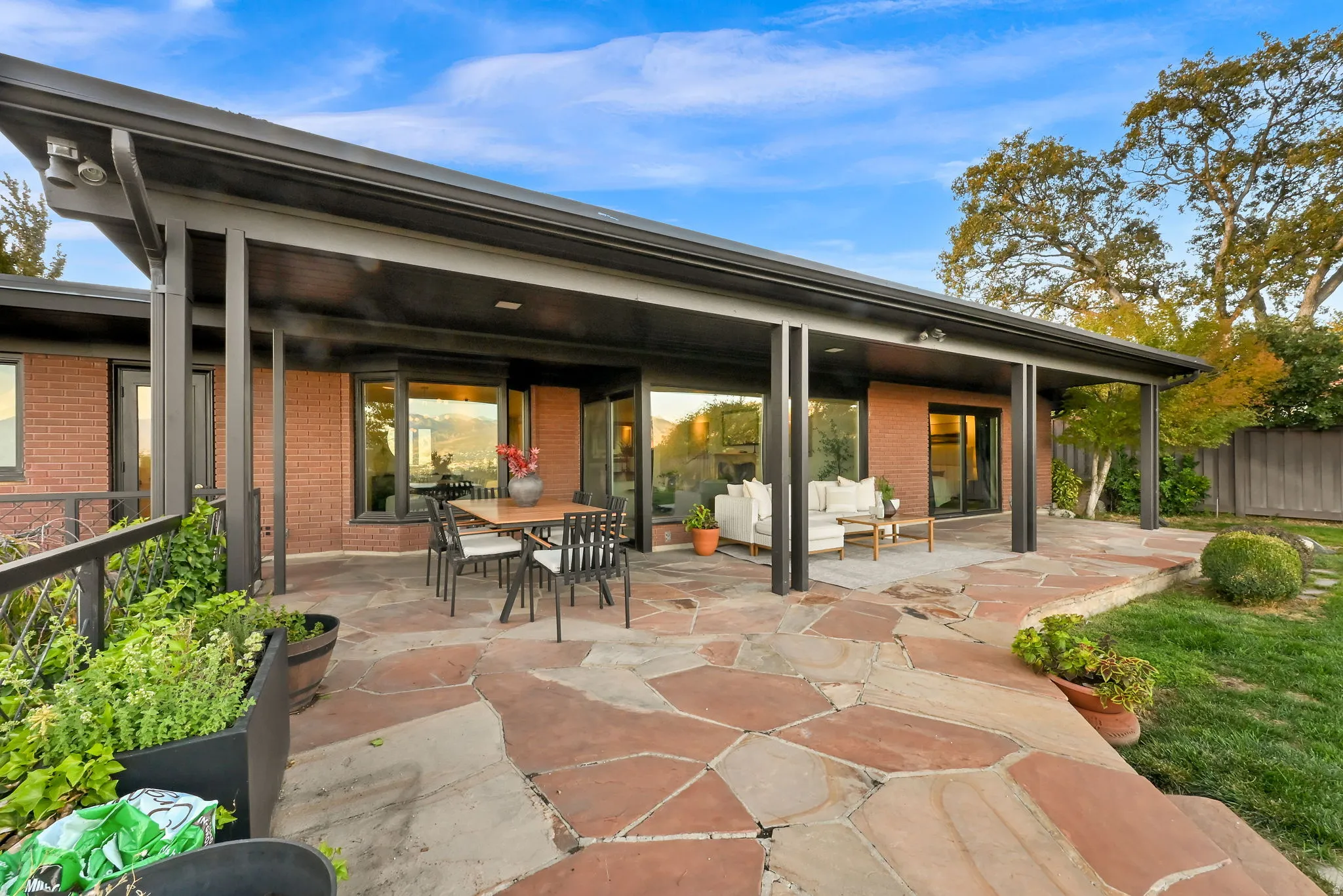 Expansive flagstone patio with a covered outdoor living area, featuring a brick exterior and multiple large windows