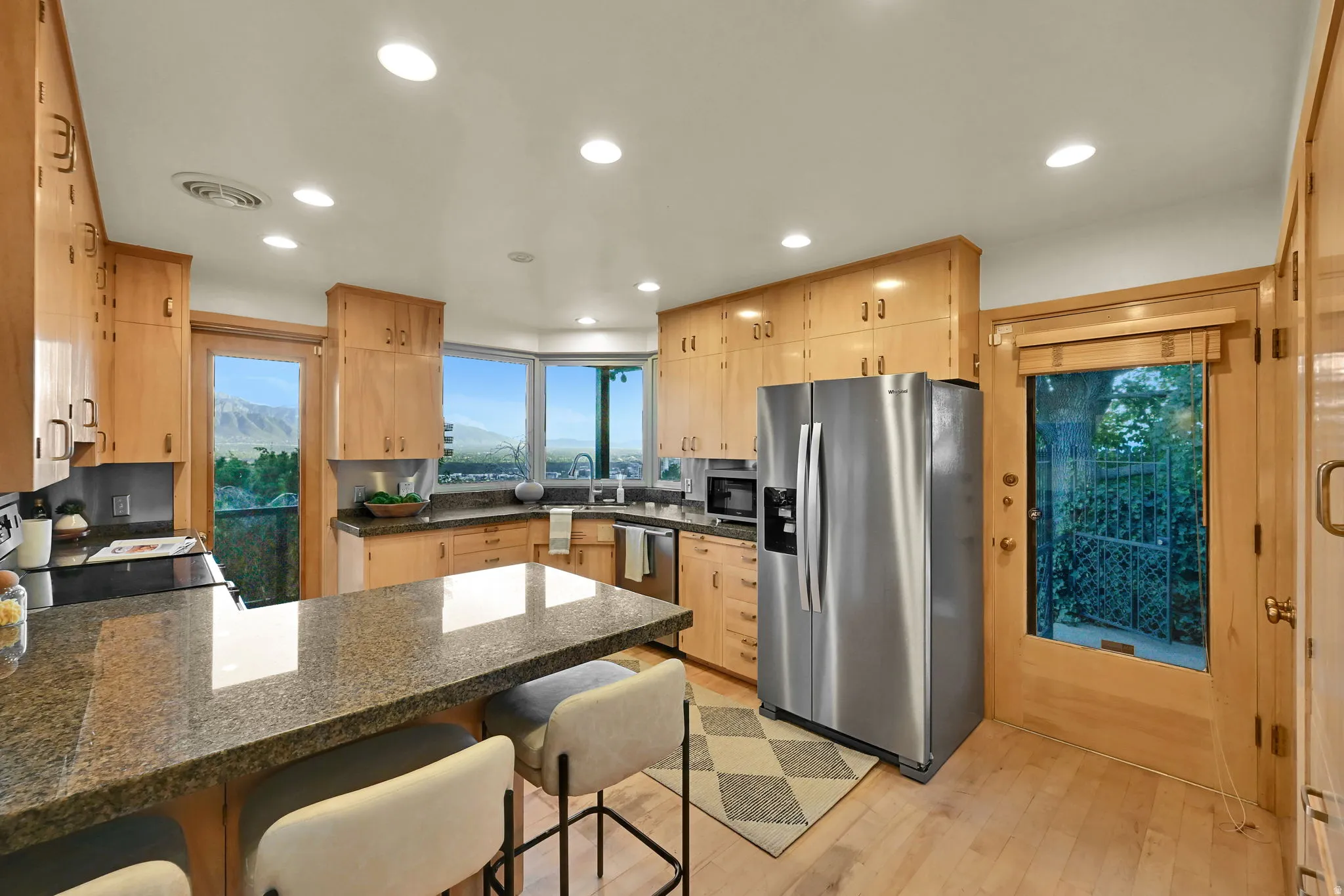 Hardwood-style flooring, ample wood cabinetry, recessed lighting, and a stainless steel refrigerator