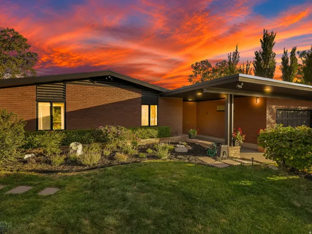 Brick exterior with dark trim accents, covered entryway with recessed lighting, integrated garage with a modern door, landscaped front yard, and a stone-paver walkway