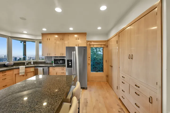 Kitchen featuring abundant light wood cabinetry, stainless steel appliances, a large center island with a stone countertop, and a built-in storage wall