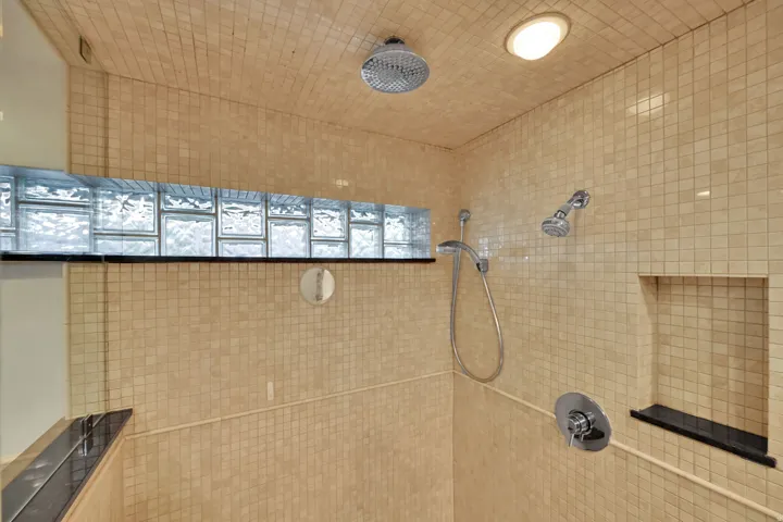 Shower featuring full-height mosaic tile, recessed lighting, glass block window, built-in shelf, and dual shower heads