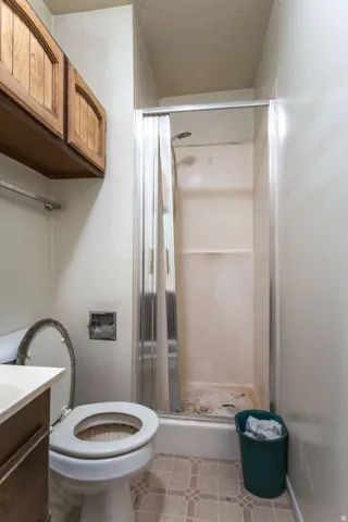 Built-in wood cabinetry, compact shower enclosure with sliding glass door, white toilet, and patterned vinyl flooring