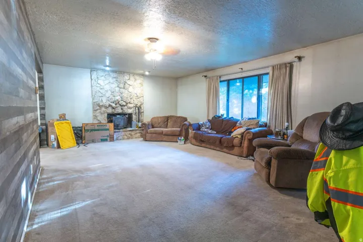Stone fireplace with hearth, wood-paneled accent wall, and ceiling fan with light fixture