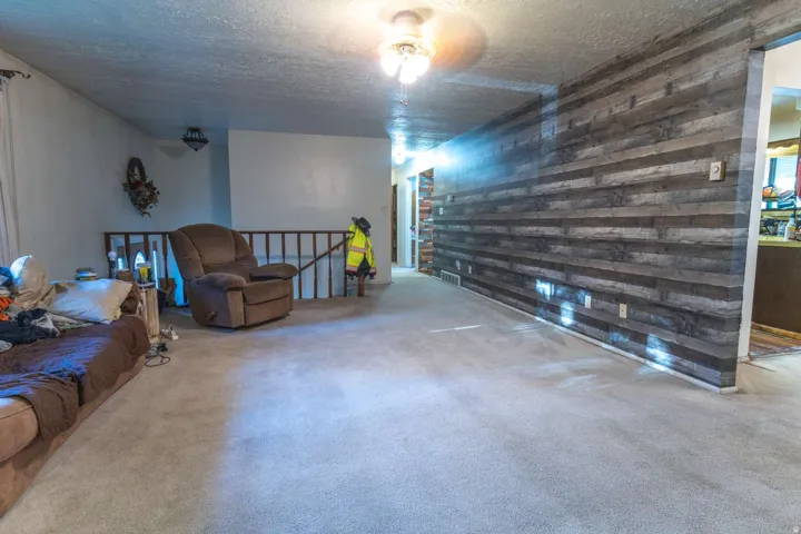 Carpeted flooring, wood-finish accent wall, ceiling-mounted light fixture, white painted walls, and a wood railing