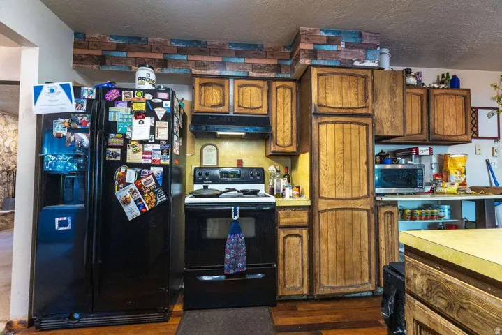 Wood-finish cabinetry, black range, black refrigerator, and wood-finish flooring