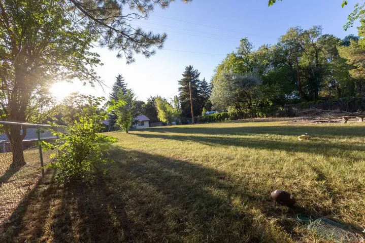 Expansive grassy area with mature trees and a chain-link fence