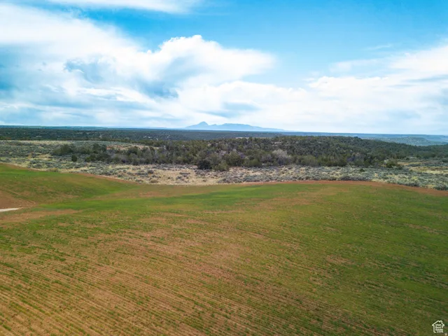 Expansive land featuring cultivated fields, natural foliage, and distant mountains under a broad sky