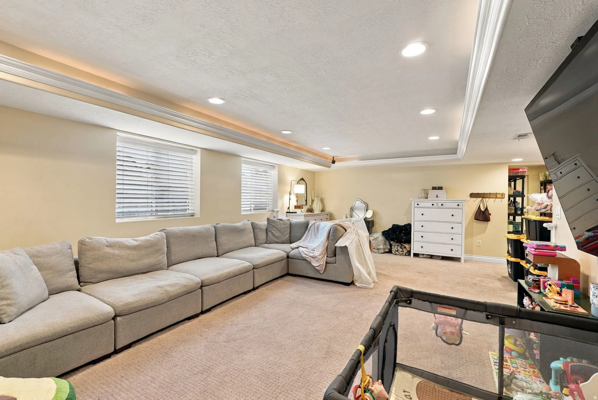 Recessed lighting, crown molding, tray ceiling, two windows with blinds, and carpeted flooring