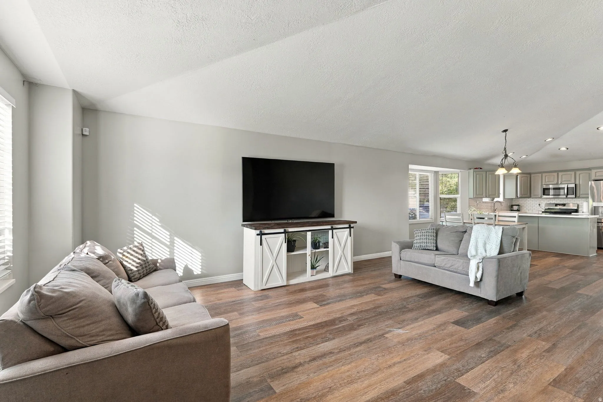 Open-concept living space featuring wood-finish flooring, recessed lighting, and a modern kitchen with a large island and stainless steel appliances
