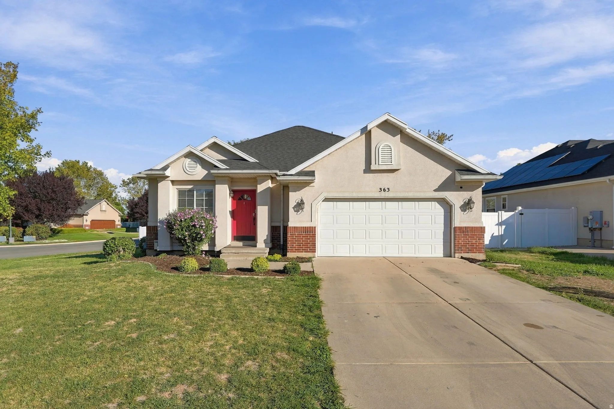 Stucco exterior with brick accents, attached garage, concrete driveway, and a red entry door